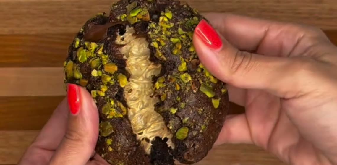 Hands opening a pistachio-stuffed cookie to reveal the molten filling
